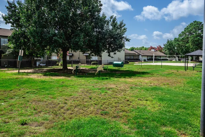 Charming fenced dog park with lush greenery and playful exercise stations, nestled within a tranquil community setting.