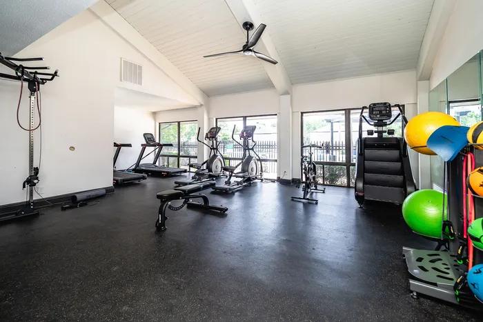 Spacious apartment gym with modern exercise equipment, bright natural light, and vibrant fitness accessories.