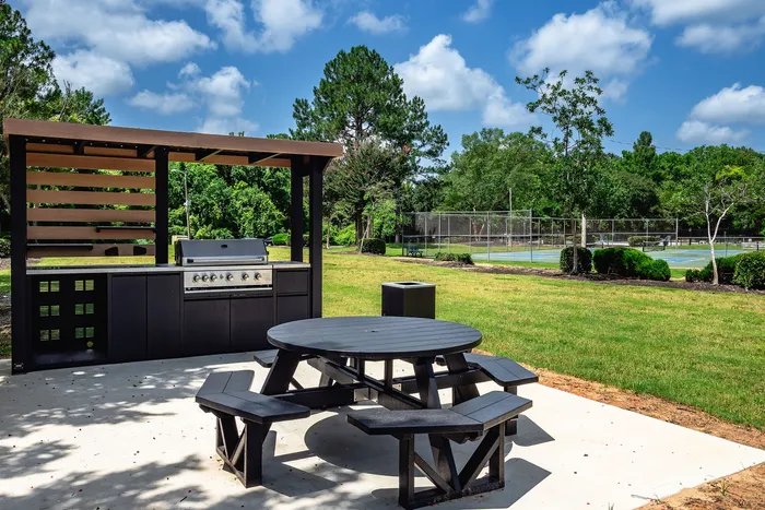 Charming outdoor area with a modern grill, shaded seating, and nearby tennis court, ideal for entertaining and recreation.