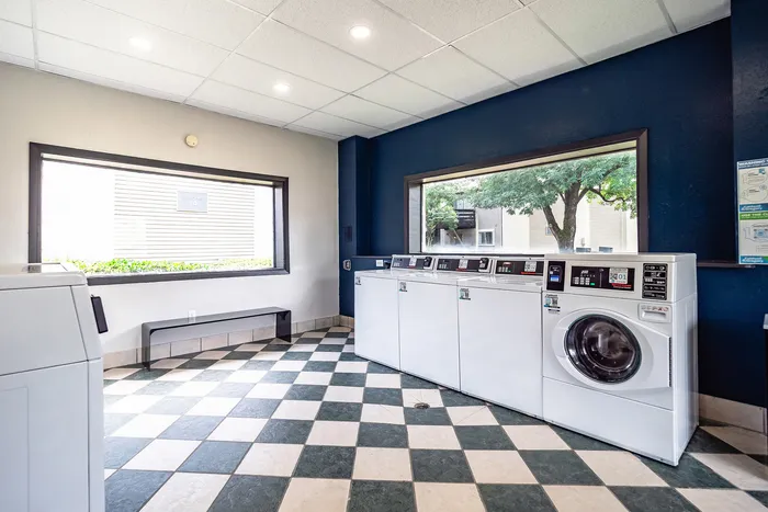 Modern laundry room featuring sleek washing machines, large windows bringing in natural light, and stylish checkered flooring.