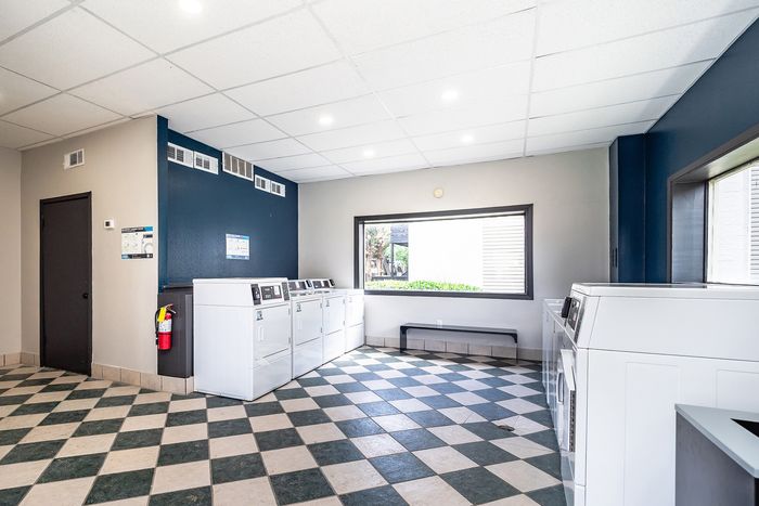Bright and spacious laundry room with modern washers and dryers, checkerboard flooring, and a large window for natural light.