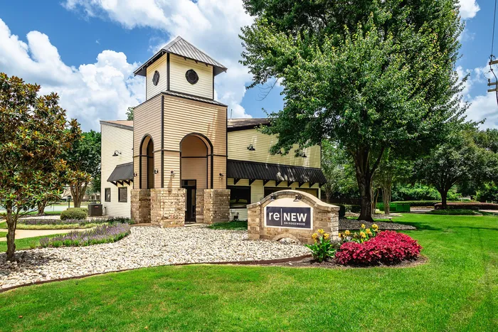 Charming apartment complex entrance with distinctive architecture, lush landscaping, and inviting signage under a clear blue sky.