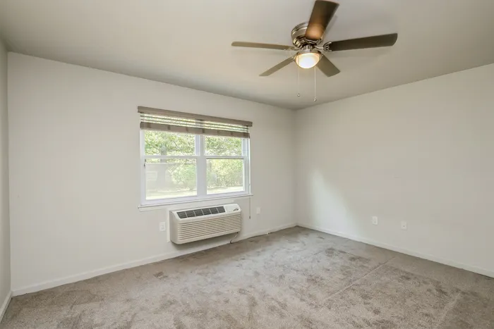 Bright and airy bedroom with plush carpeting, large window, and ceiling fan, perfect for comfort and relaxation.