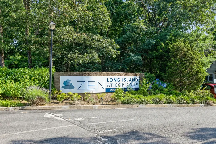Inviting entrance sign for Zen Long Island at Copiague, surrounded by lush greenery and vibrant flowers, highlighting a serene environment.
