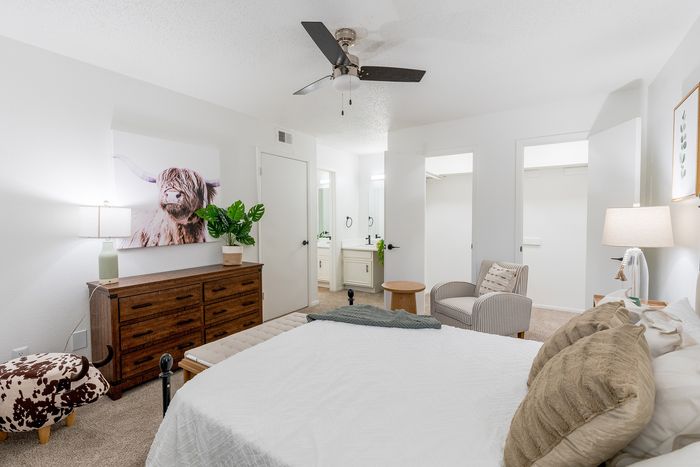 Inviting bedroom with cozy white bedding, stylish wooden dresser, and serene decor featuring a Highland cow artwork and lush potted plant.