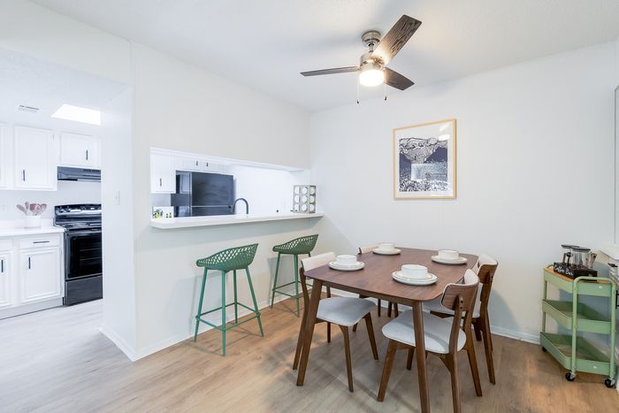 Inviting dining area with a modern wooden table set for four, adjacent to a bright, open kitchen with stylish bar seating.