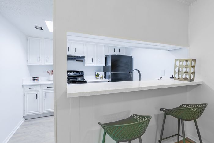 Chic modern kitchen with sleek white cabinetry, black fridge, stylish bar counter, and cozy seating.
