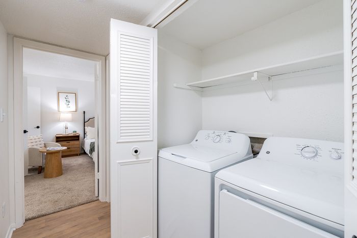 Bright laundry area with modern washer and dryer next to an inviting bedroom featuring cozy furniture and elegant decor.