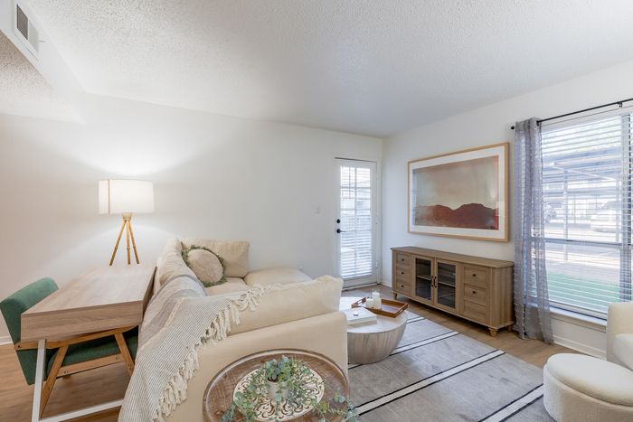 Charming living room with cozy beige sectional, elegant wooden furniture, and bright natural light through large windows.