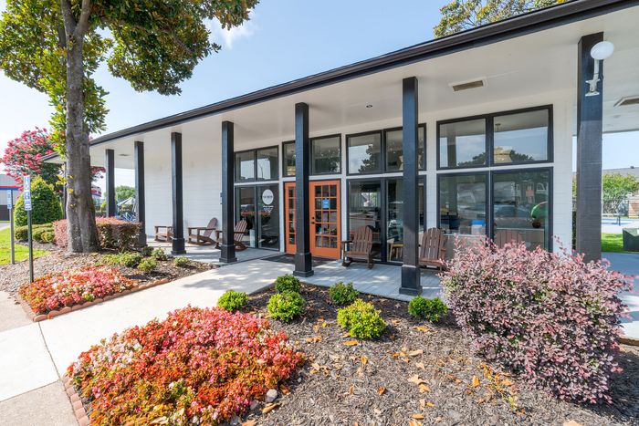 Charming building entrance with modern architecture, large glass windows, surrounded by vibrant landscaping and colorful flowers.