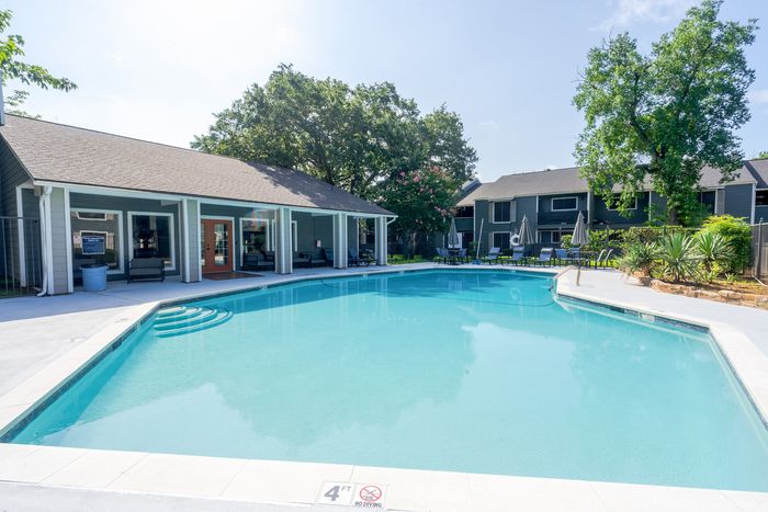 Inviting apartment complex pool area with crystal-clear water, surrounded by lush greenery and cozy seating for a relaxing retreat.
