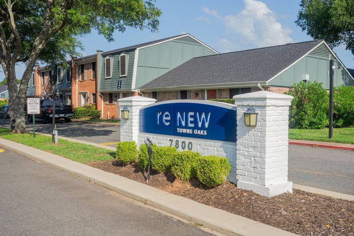 Charming townhouse community entrance with a welcoming 'reNEW Towne Oaks' sign surrounded by lush greenery.