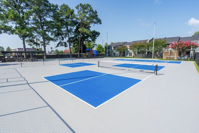 Vibrant outdoor sports court with blue and white markings, surrounded by lush greenery and modern apartments, perfect for active living.
