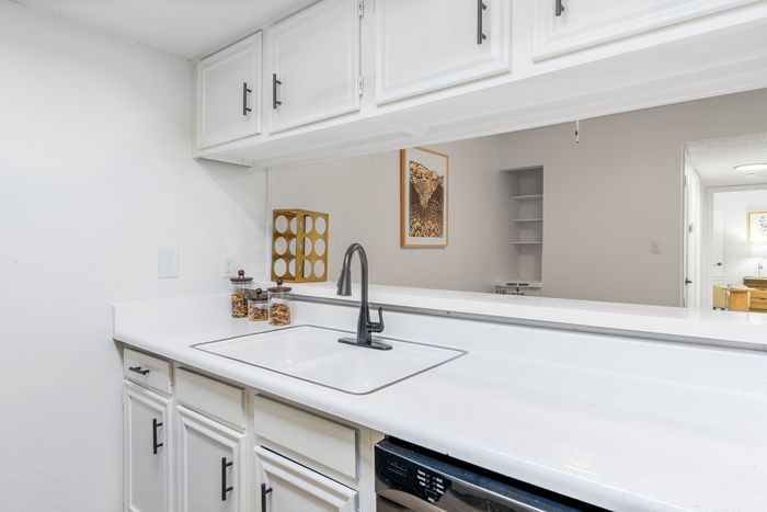 Bright, modern kitchen with sleek white cabinets, elegant black faucet, and a view into the cozy living space, perfect for entertaining.