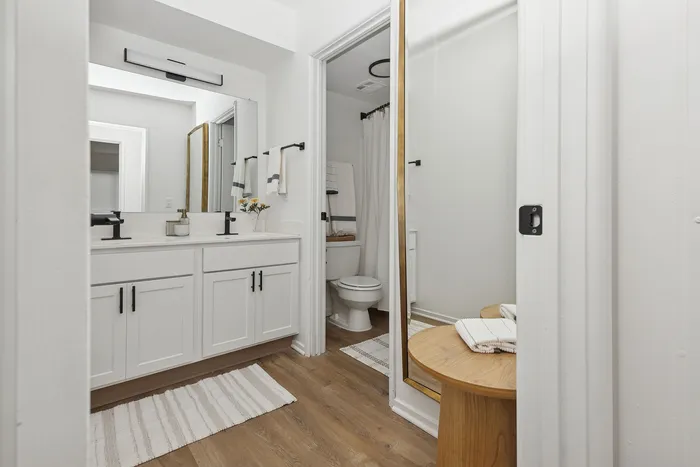 Elegant modern bathroom with sleek double sinks, stylish fixtures, and a cozy wooden side table for added charm.