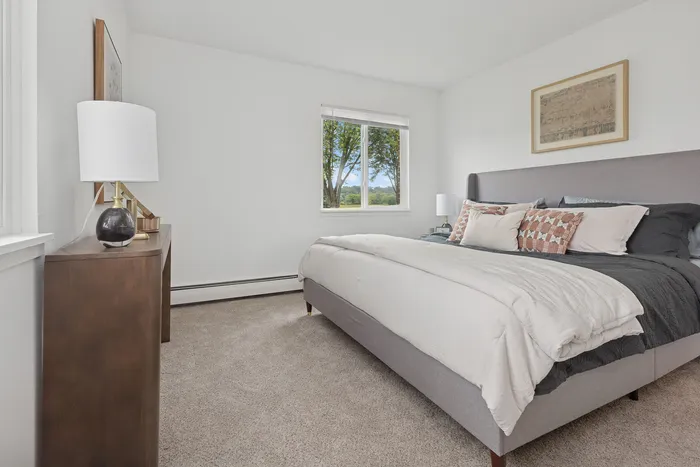 Bright, elegant bedroom with a large window offering serene views and natural light, featuring a plush bed with stylish cushions and a sleek bedside table with a modern lamp.