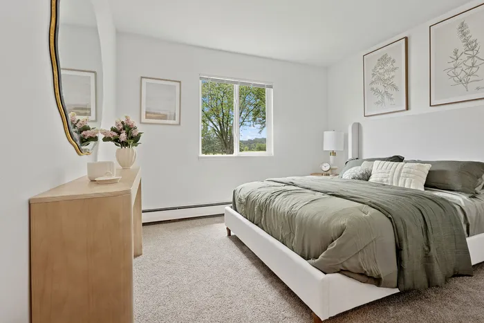 Bright and airy bedroom with elegant decor, featuring a plush bed, stylish artwork, and a scenic window view.