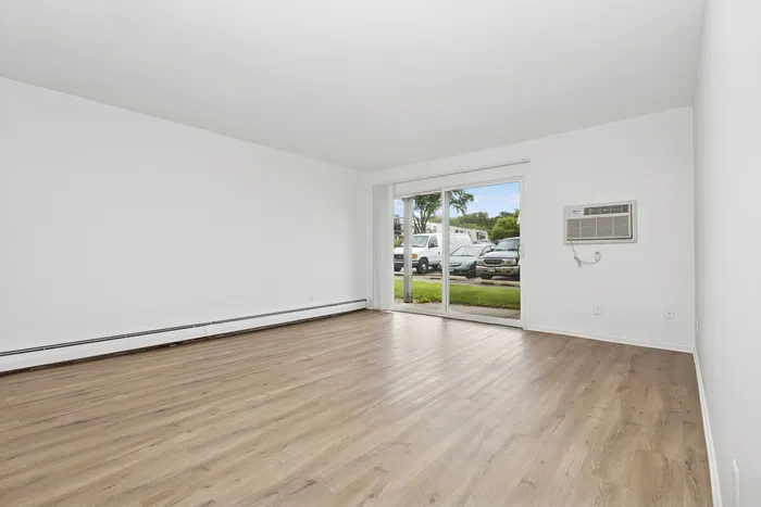 Bright and airy living room with elegant wood flooring, large sliding glass doors, and a serene view of greenery.