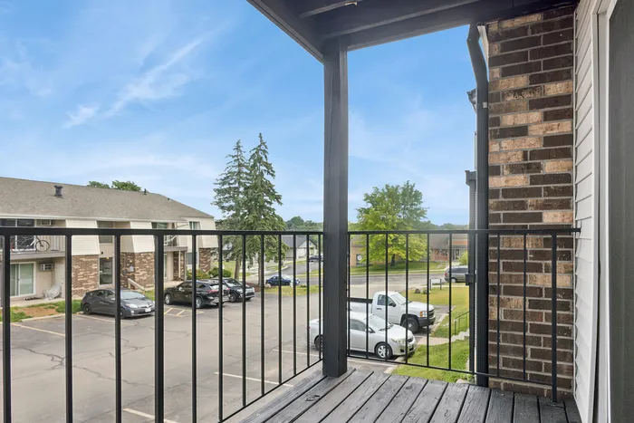 Charming apartment balcony overlooking a serene neighborhood, perfect for relaxing with a view of lush greenery and the open sky.