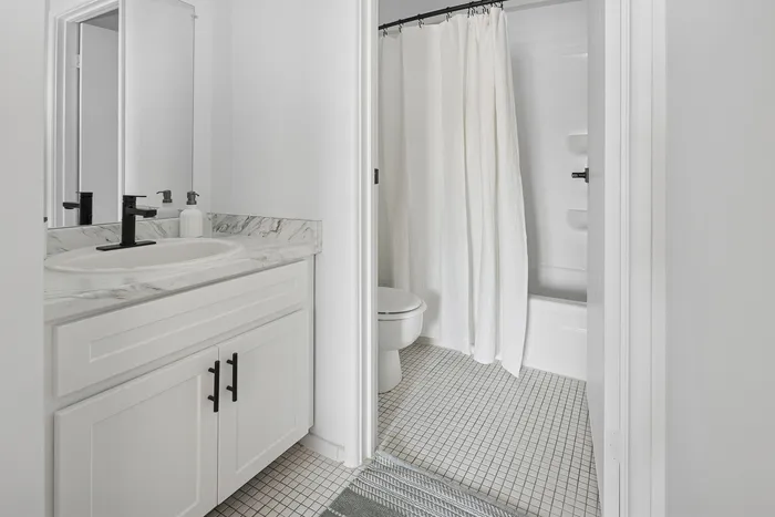 Elegant bathroom with a modern design, featuring a sleek marble countertop, stylish black fixtures, and a pristine white shower curtain, creating a tranquil and sophisticated atmosphere.