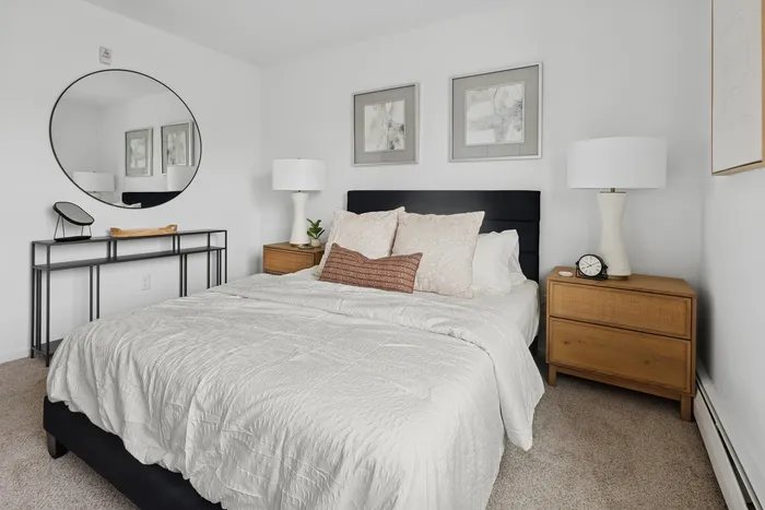 Modern bedroom with cozy queen bed, elegant decor, and stylish round mirror, offering a serene retreat.