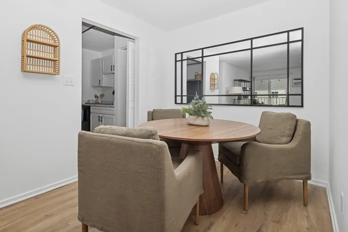 Elegant dining area with a round wooden table and plush chairs, open view to a modern kitchen, accented by a large, industrial-style wall mirror.