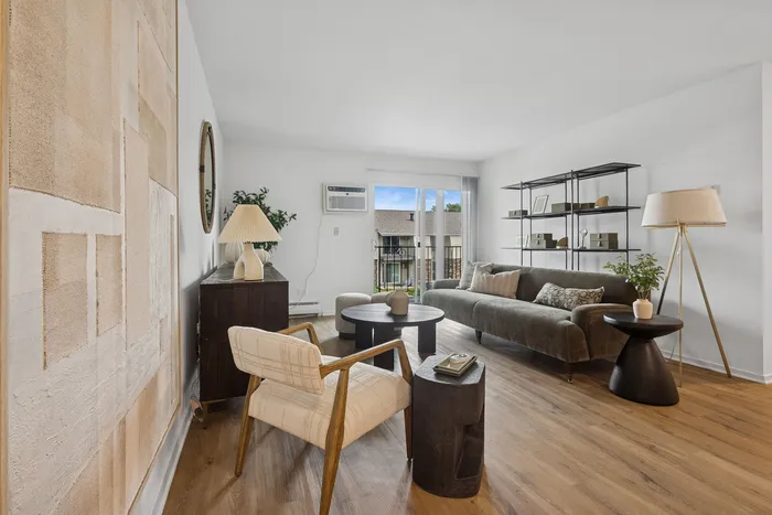Modern living room with sleek wooden flooring, featuring a chic sofa, elegant decor, and abundant natural light through large windows.