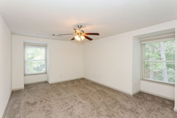 Bright, spacious bedroom with plush carpet, ceiling fan, and large windows offering lush views.