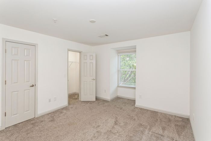 Bright and inviting bedroom with plush carpeting, spacious walk-in closet, and a large window showcasing greenery.