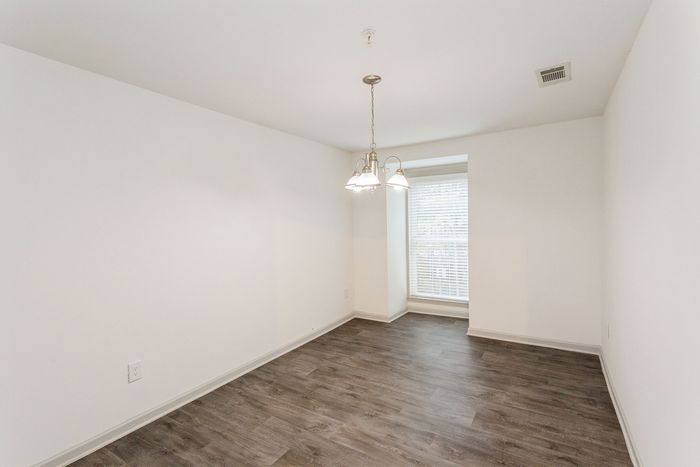 Bright dining area with modern lighting fixture and elegant wood flooring, complemented by natural light through large window.