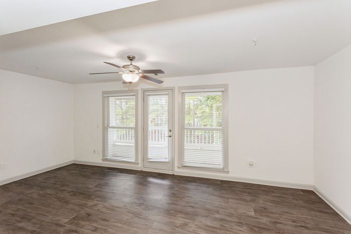 Bright and airy living room with elegant wood flooring and large windows providing lush greenery views.