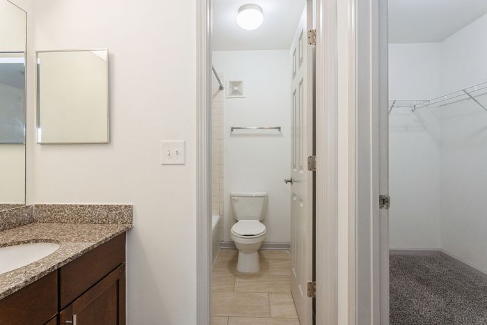 Bright and modern bathroom with polished granite countertop, spacious walk-in closet, and pristine tile flooring.