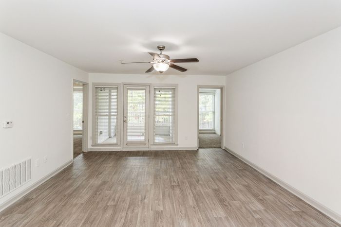 Bright and spacious living area with sleek wooden flooring, ceiling fan, and access to balcony through elegant French doors.