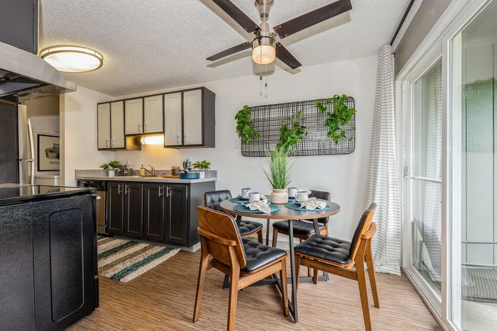 Chic dining area with modern wooden furniture and lush greenery, adjacent to a sleek kitchen with stylish cabinetry.