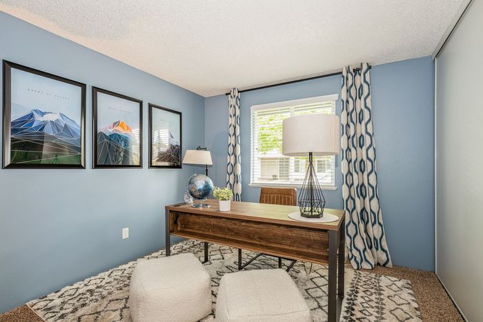 Charming home office with modern artwork and a large window, featuring a wooden desk and cozy seating.
