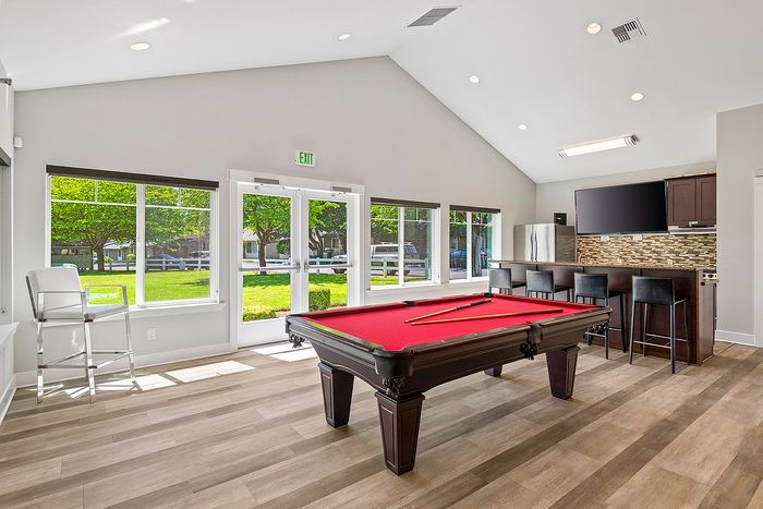 Bright recreational room featuring a red pool table, modern bar seating, and expansive windows with garden views.