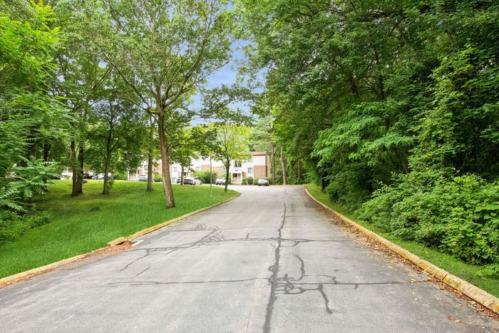 Charming residential entrance with lush green trees and well-maintained road leading to cozy homes in a serene neighborhood.