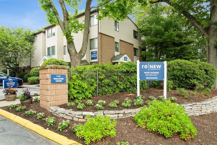 Charming apartment complex surrounded by lush greenery, featuring a welcoming sign and inviting garden path, ideal for new residents seeking a serene community.