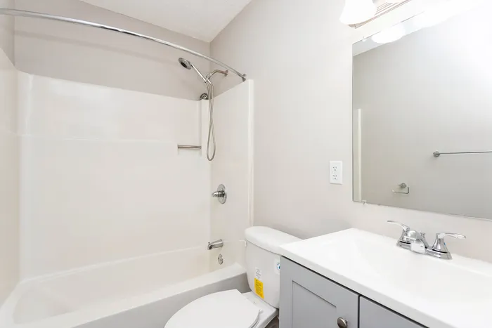 Modern bathroom featuring a sleek bathtub with a curved curtain rod, pristine white vanity with mirror, and stylish fixtures.