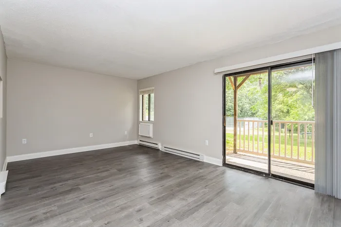 Bright and spacious living room with elegant hardwood floors, large window, and sliding glass doors leading to a serene outdoor view.