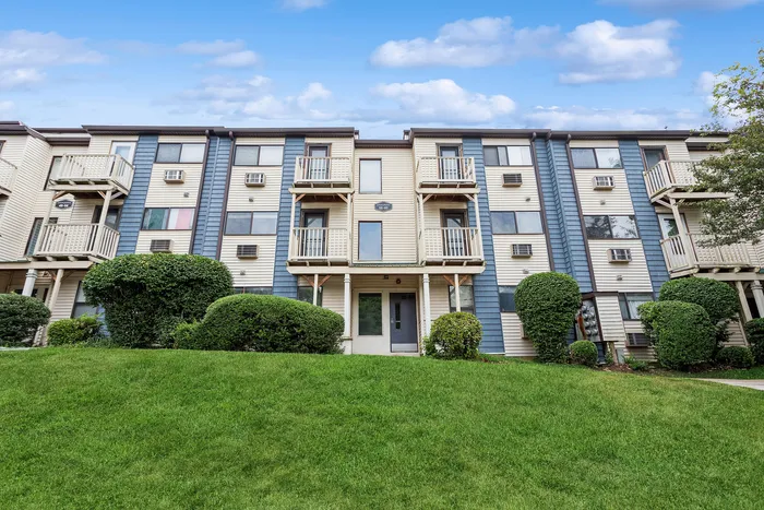 Charming three-story apartment building with private balconies, manicured hedges, and a lush green lawn, offering a welcoming atmosphere.