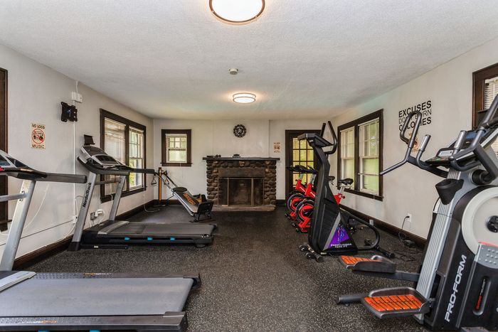 Inviting fitness room featuring state-of-the-art exercise equipment, including treadmills and stationary bikes, with a cozy rustic fireplace backdrop.