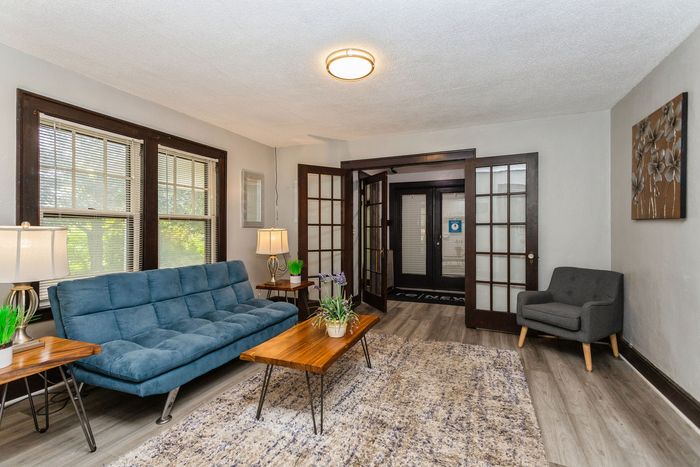 Inviting living room with stylish French doors, cozy teal sofa, elegant wooden coffee table, and ample natural light, perfect for relaxation.