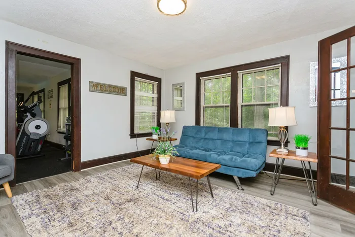 Inviting living room with a cozy blue sofa, elegant wooden coffee table, and plentiful natural light, leading to a modern exercise space.