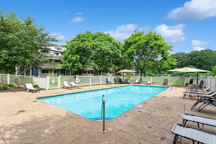 Inviting outdoor swimming pool surrounded by comfortable lounge chairs and lush green trees, perfect for relaxation in a serene apartment community.