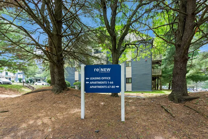 Serene apartment complex entrance surrounded by lush greenery, featuring a clear directional sign for leasing office and apartments.
