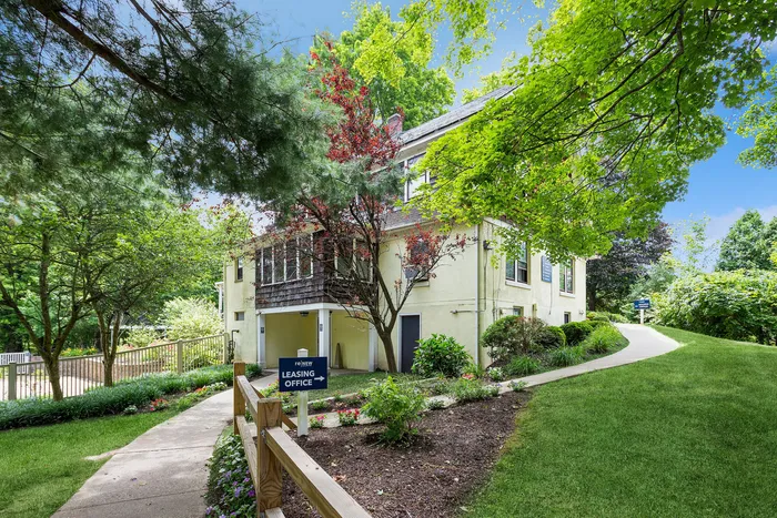 Charming apartment building surrounded by lush greenery and vibrant landscaping, featuring a welcoming leasing office entrance.