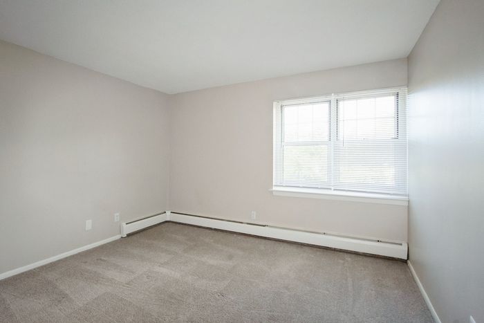 Bright and spacious bedroom with soft carpet flooring, neutral walls, and a large window inviting natural light.