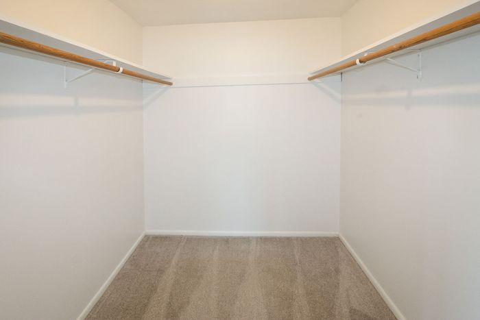 Spacious walk-in closet with elegant wooden hanging rods and plush carpet flooring.