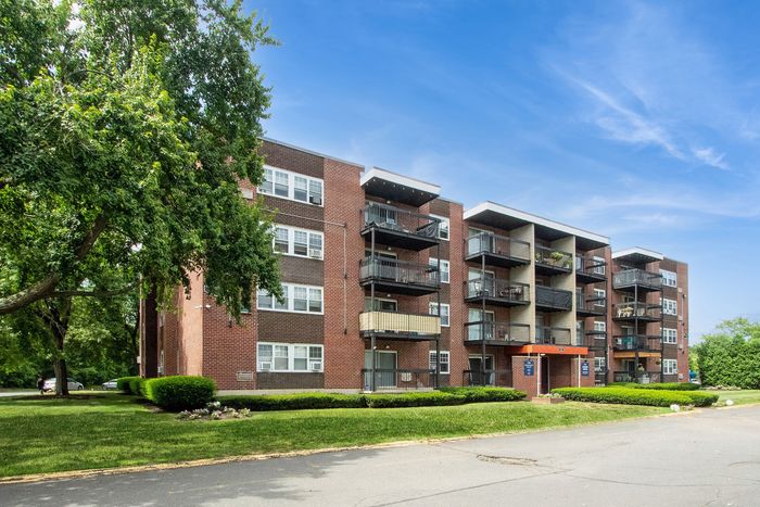 Charming brick apartment building with spacious balconies, surrounded by lush greenery and idyllic outdoor space.